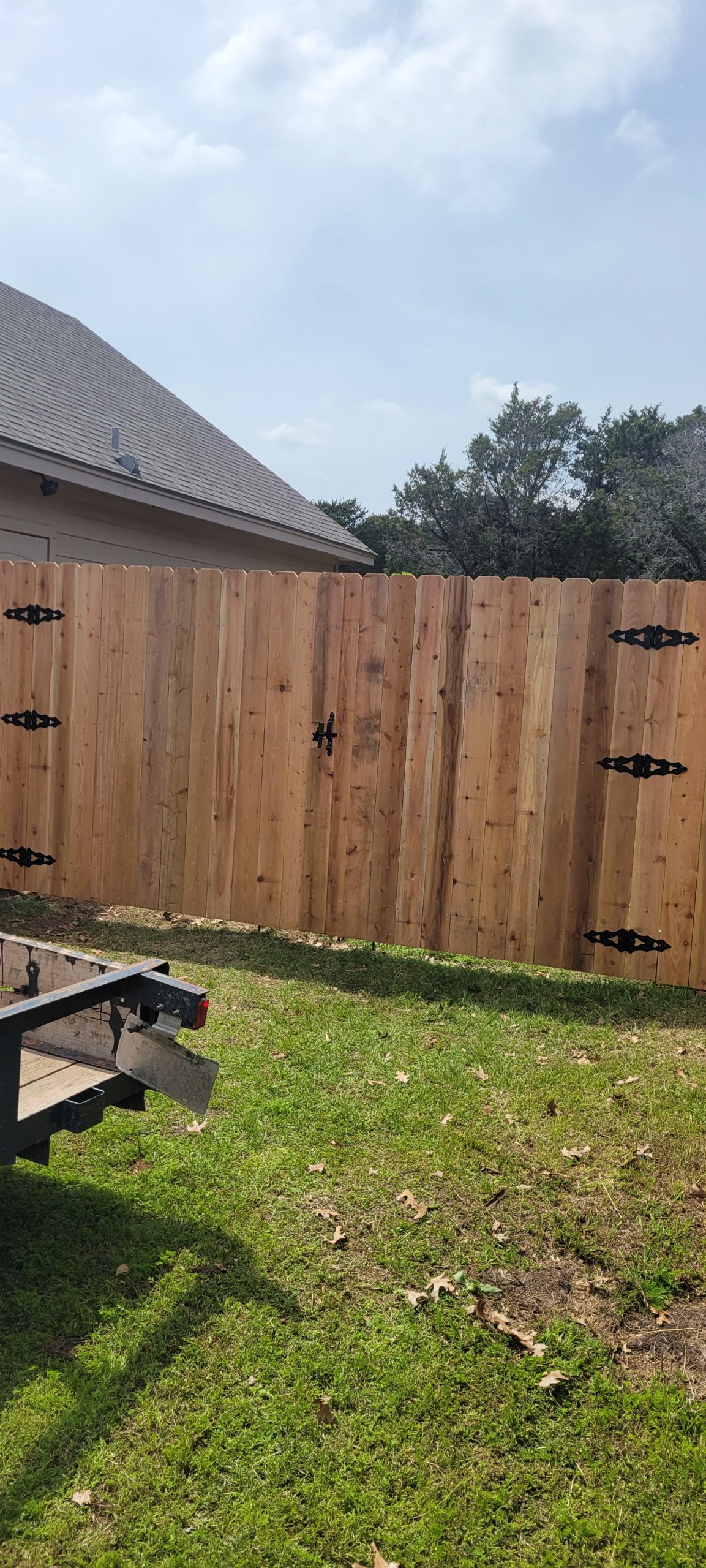Freshly repaired cedar wood fence gate with new decorative black hinges and hardware