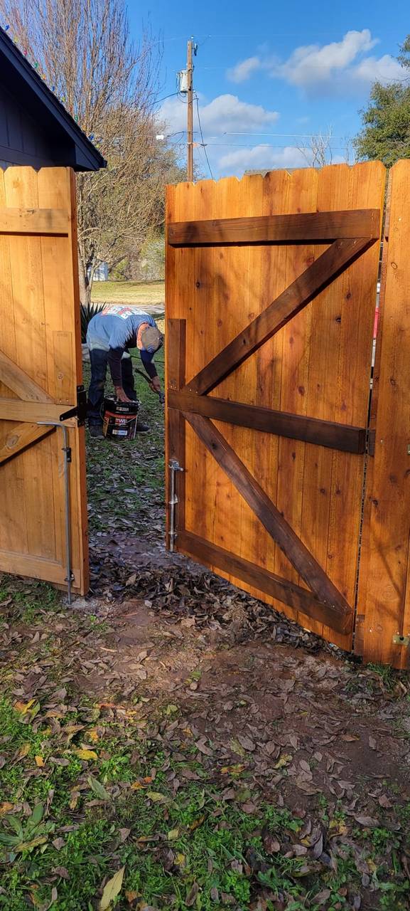 All Around Fencing crew member staining a newly built cedar wood gate on a Granbury-area property