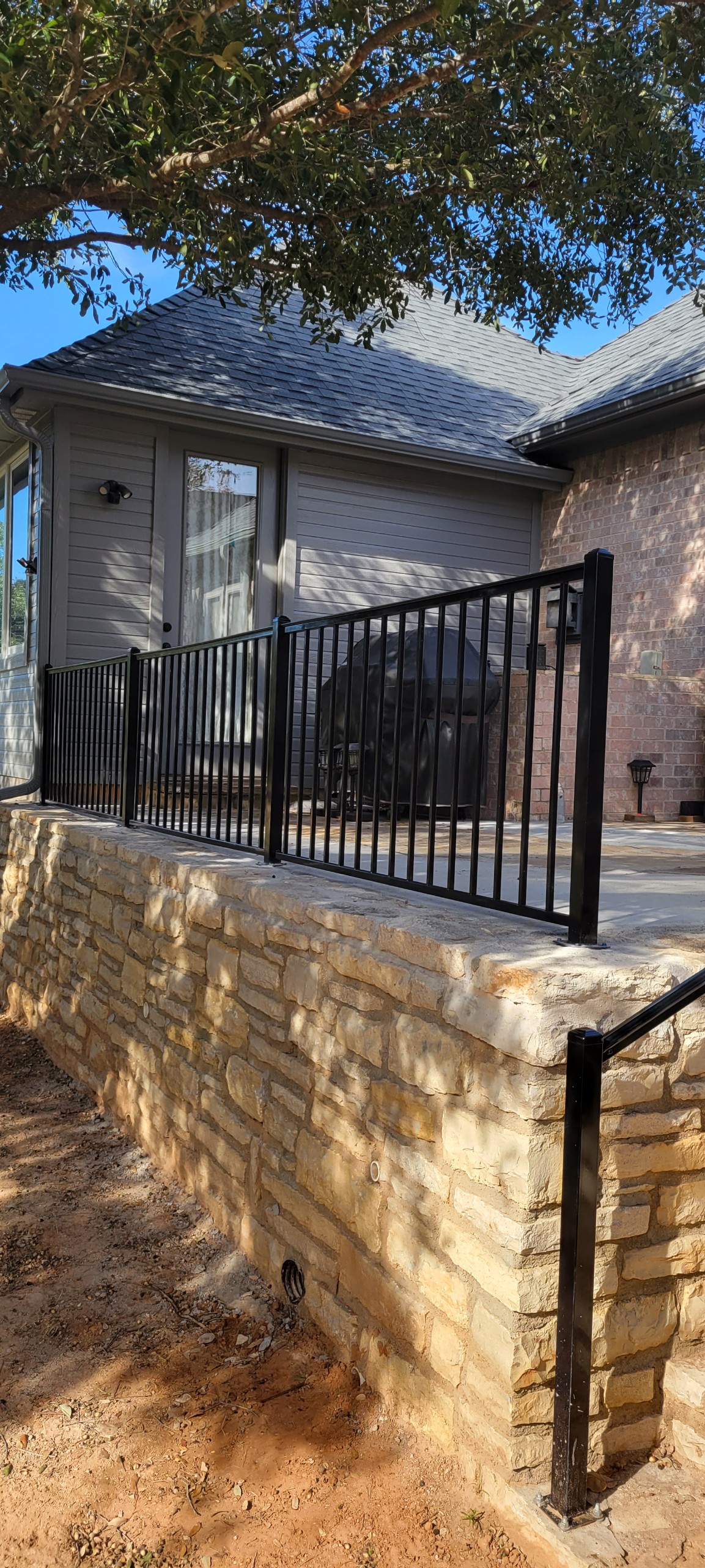Black ornamental metal railing atop a stacked-stone wall beside a Granbury-area home