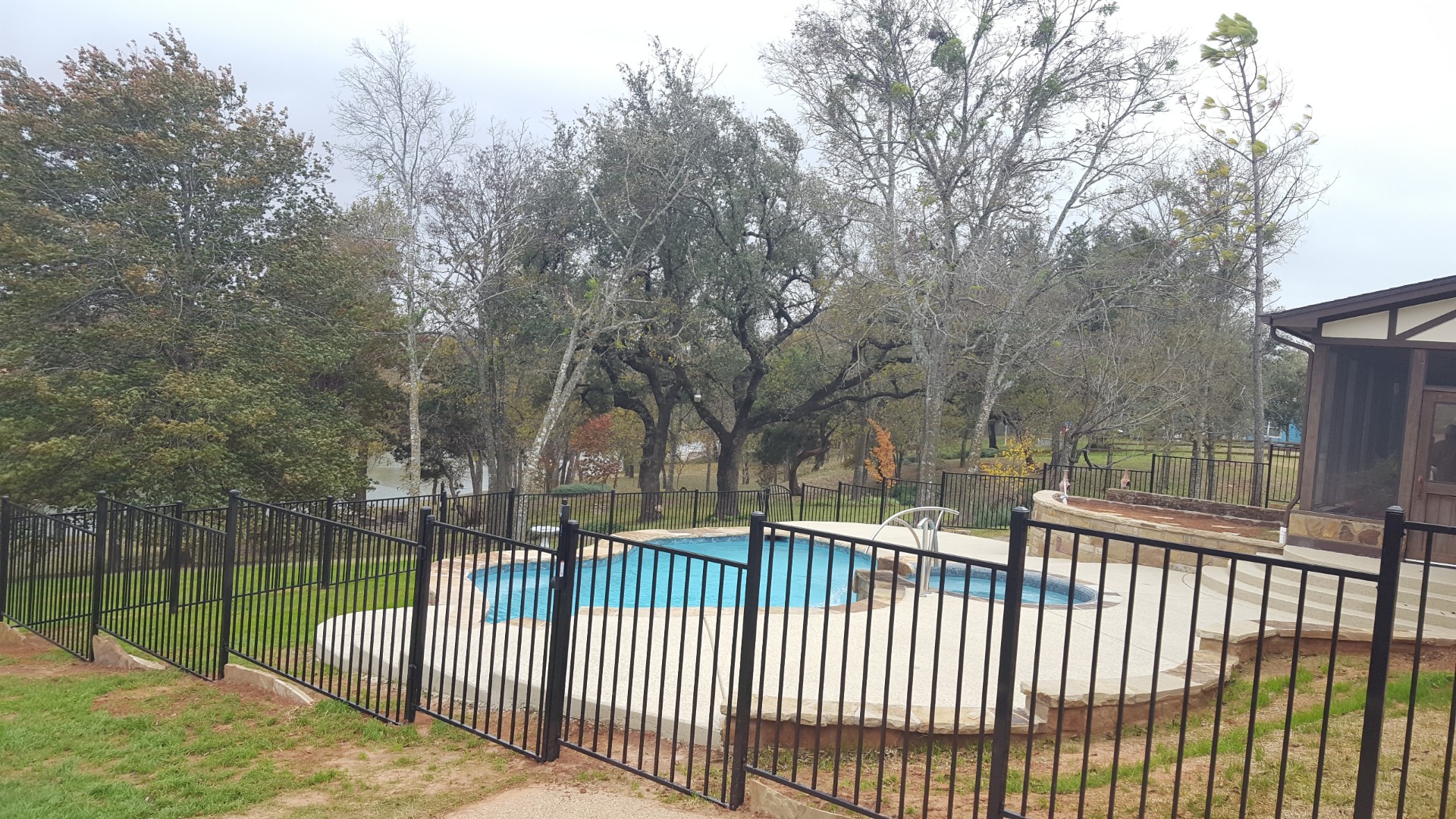Black ornamental metal fence enclosing a backyard pool with Lake Granbury visible beyond the yard