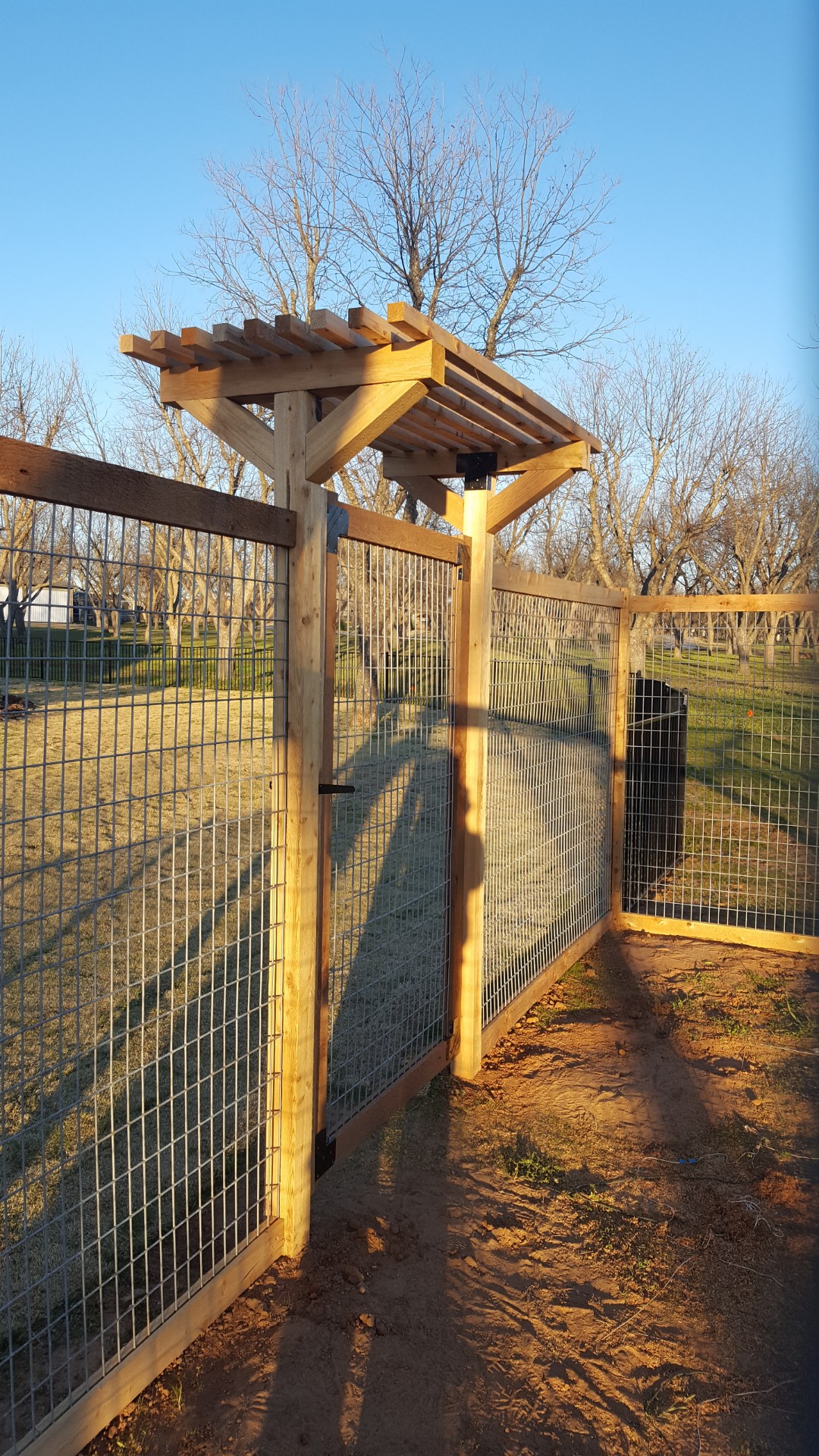 Cedar wood pergola-topped gate with hog wire fencing on a Hood County property