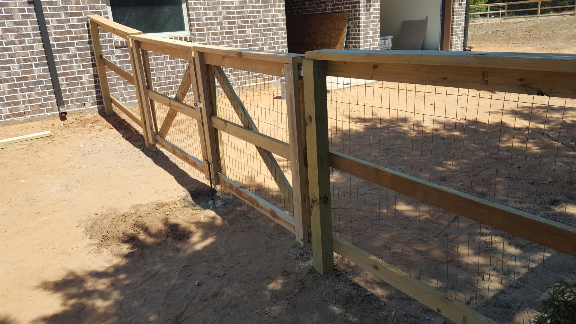 Wood and wire farm fence with gate built against a brick home on a rural Hood County property