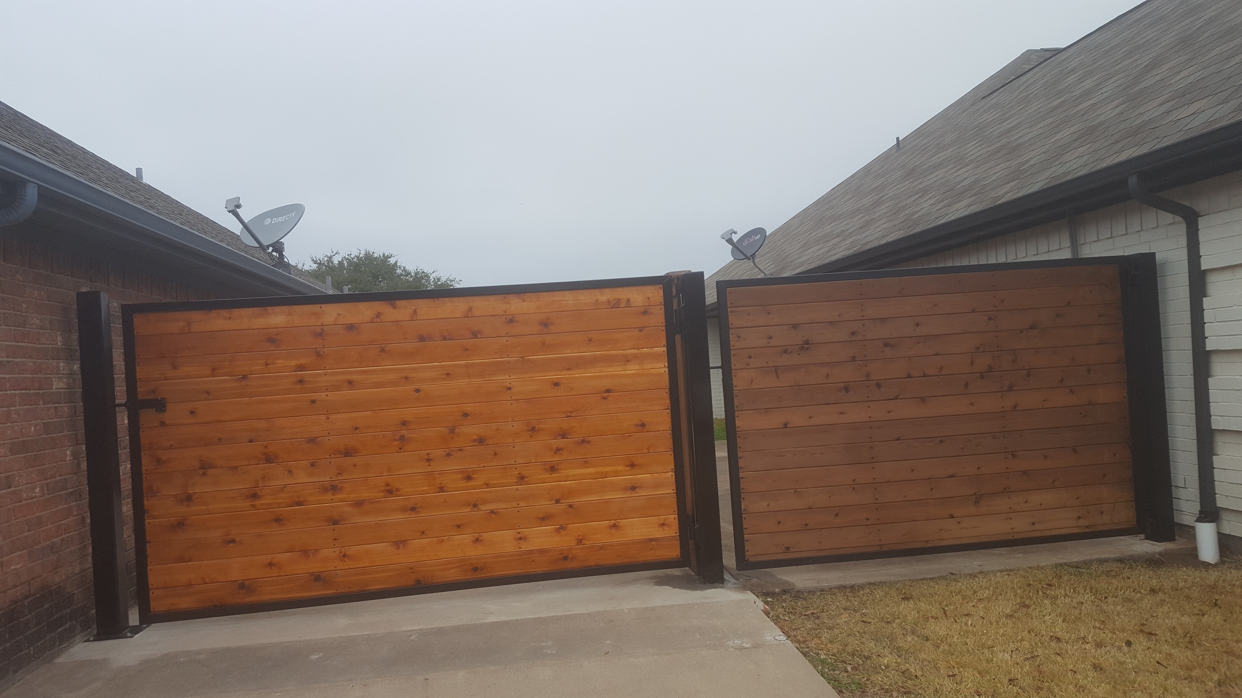 Custom double driveway gate with cedar panels and a black metal frame built by All Around Fencing