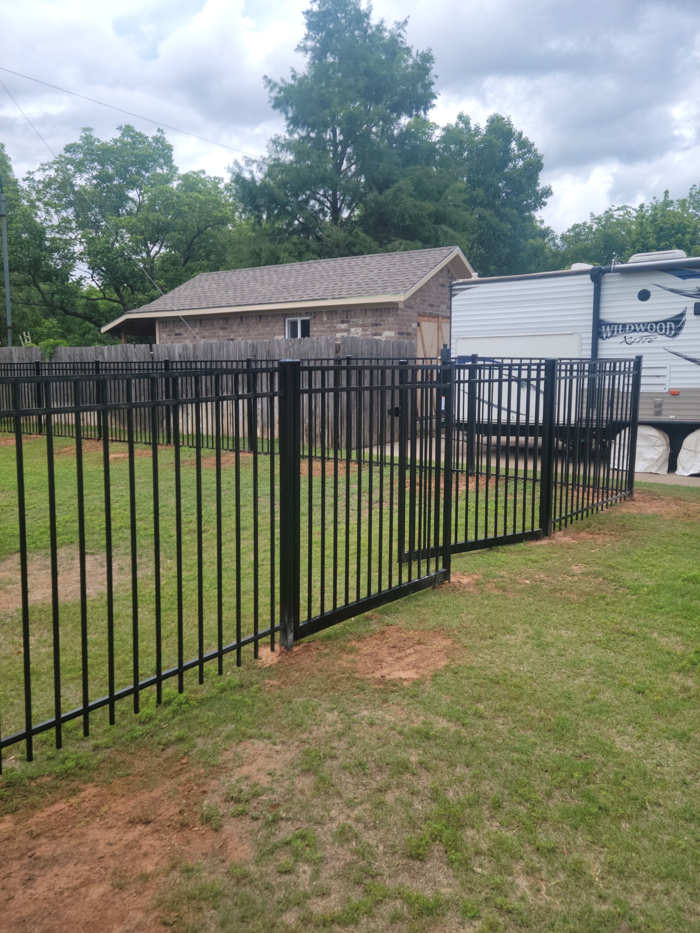 Black metal fence and gate installed beside a storage building on a rural Hood County property