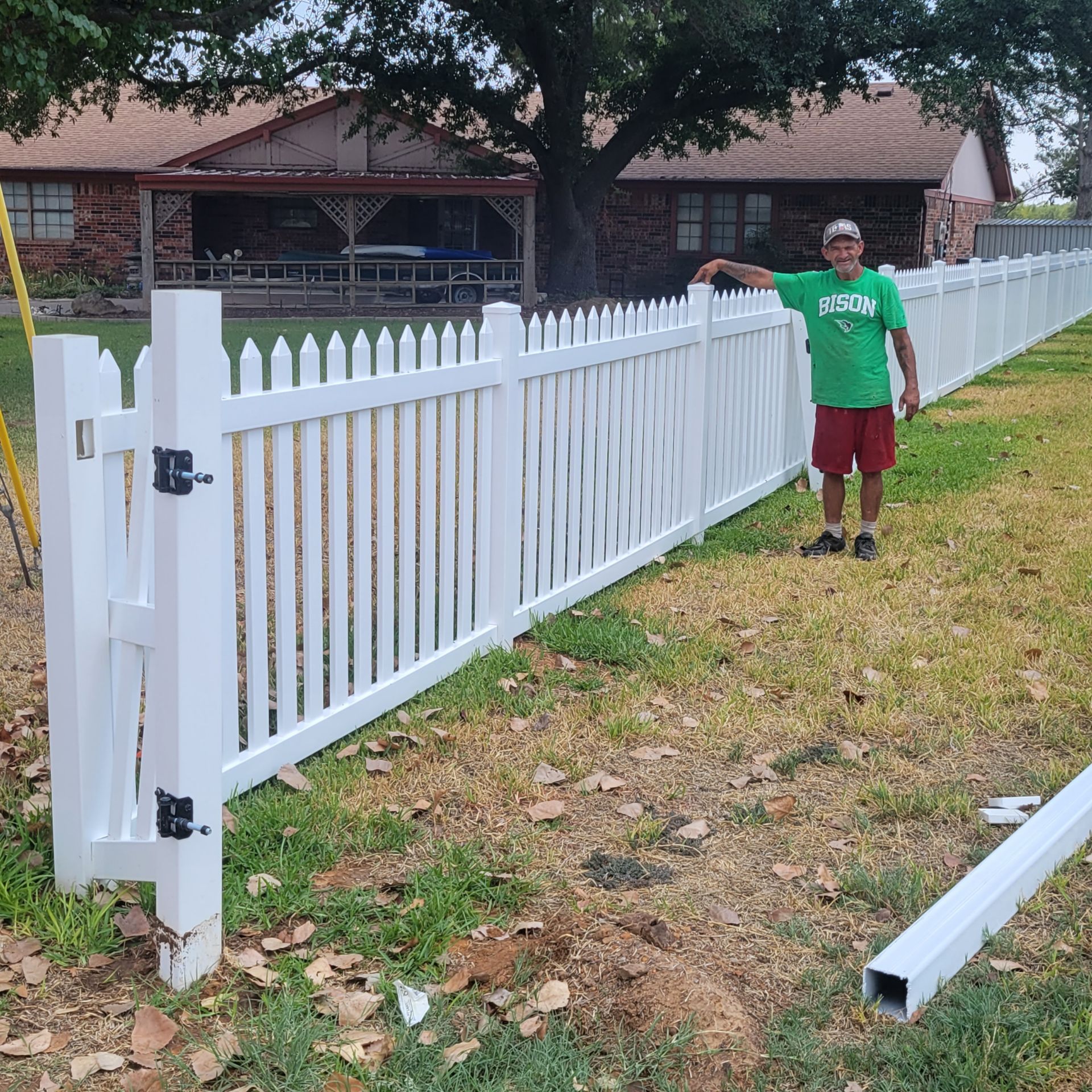 All Around Fencing crew member standing beside a freshly installed white vinyl picket fence and gate