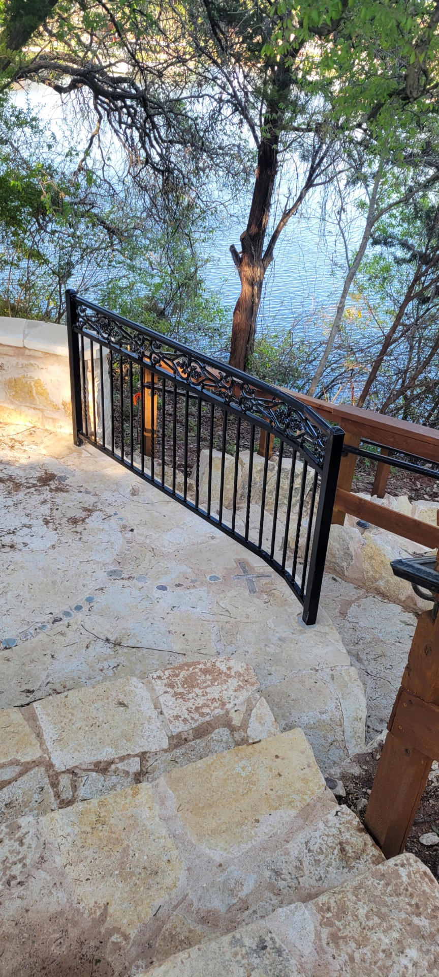 Black ornamental iron gate with scrollwork detail at the top of a stone patio on a Lake Granbury property
