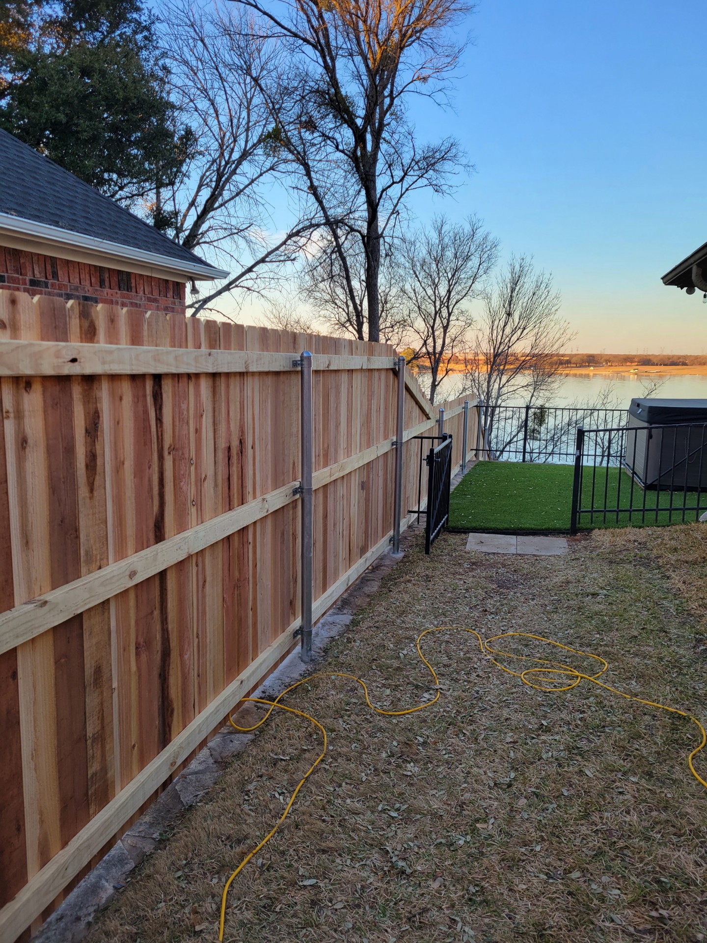 New cedar privacy fence with a turf dog run and metal gate installed on a Lake Granbury-area backyard