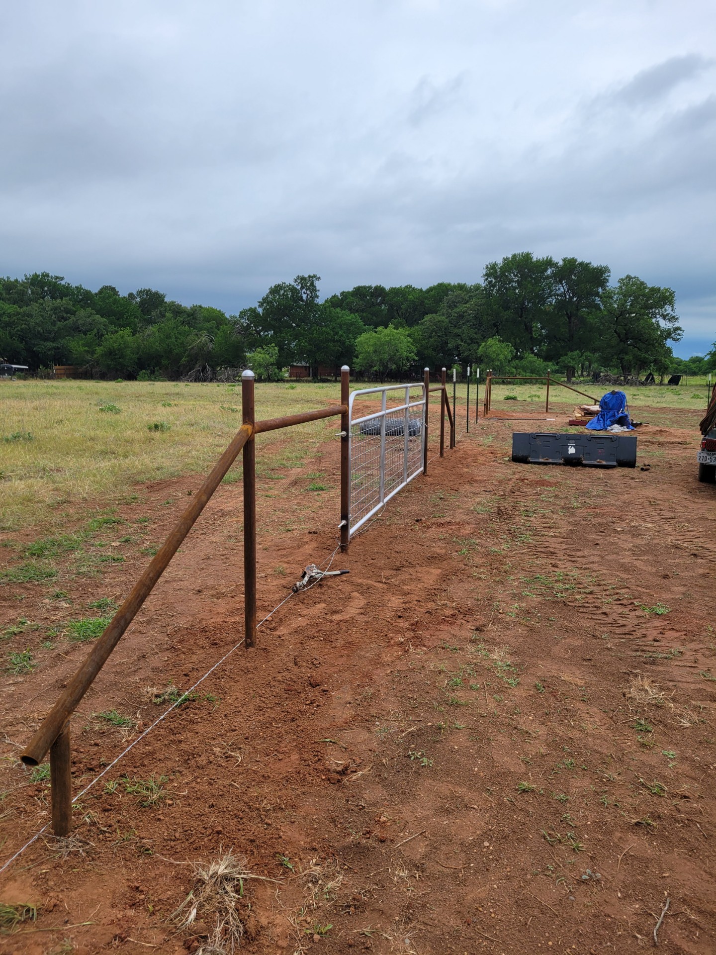 Pipe fence line and metal gate under construction on a rural Hood County ranch property